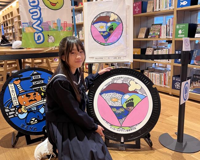 展示されているマンホール蓋と原画、近藤さんが写っている様子